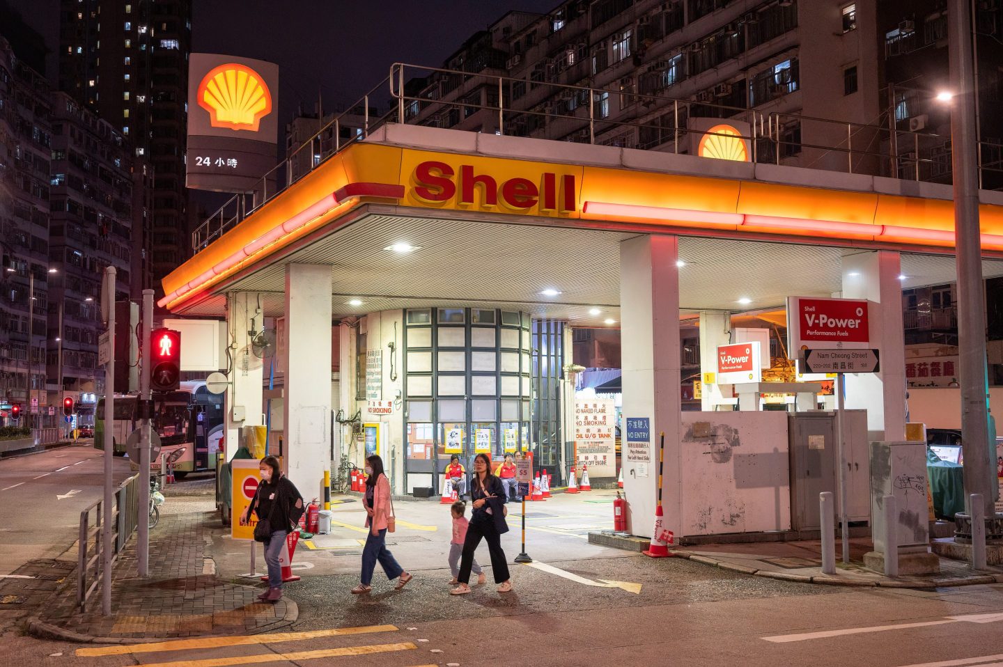 Pedestrians walk past a Shell garage at night