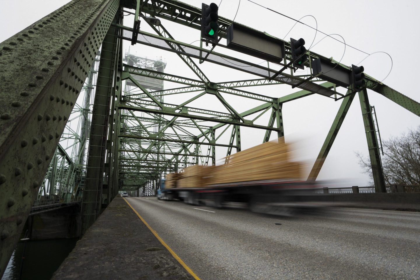 FILE &#8211; A logging truck drives on the Interstate 5 bridge that spans the Columbia River and connects Portland, Ore., with southwest Washington state, Feb. 13, 2024. Dozens of aging bridges, including this Interstate 5 bridge, in 16 states will be replaced or improved with the aid $5 billion of federal grants announced Wednesday, July 17, by President Joe Biden&#8217;s administration as the latest beneficiaries of a massive infrastructure law. (AP Photo/Jenny Kane, File)