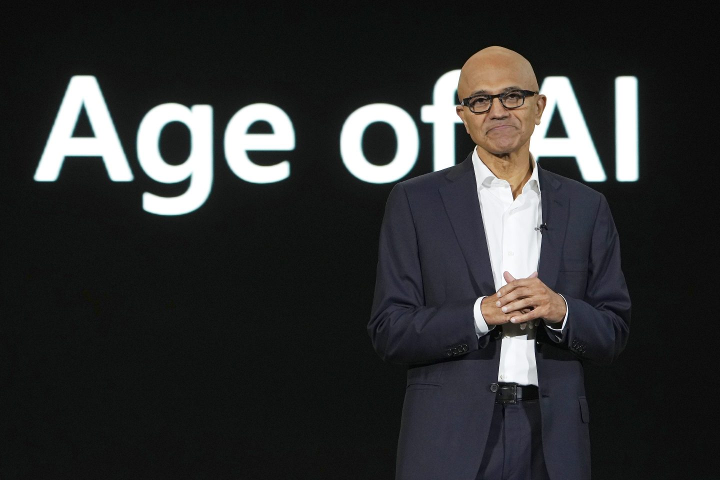 Microsoft CEO Satya Nadella stands in front of a screen that says "Age of AI"
