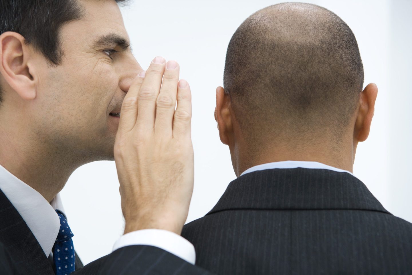 A man in a suit whispering to another man in a suit.