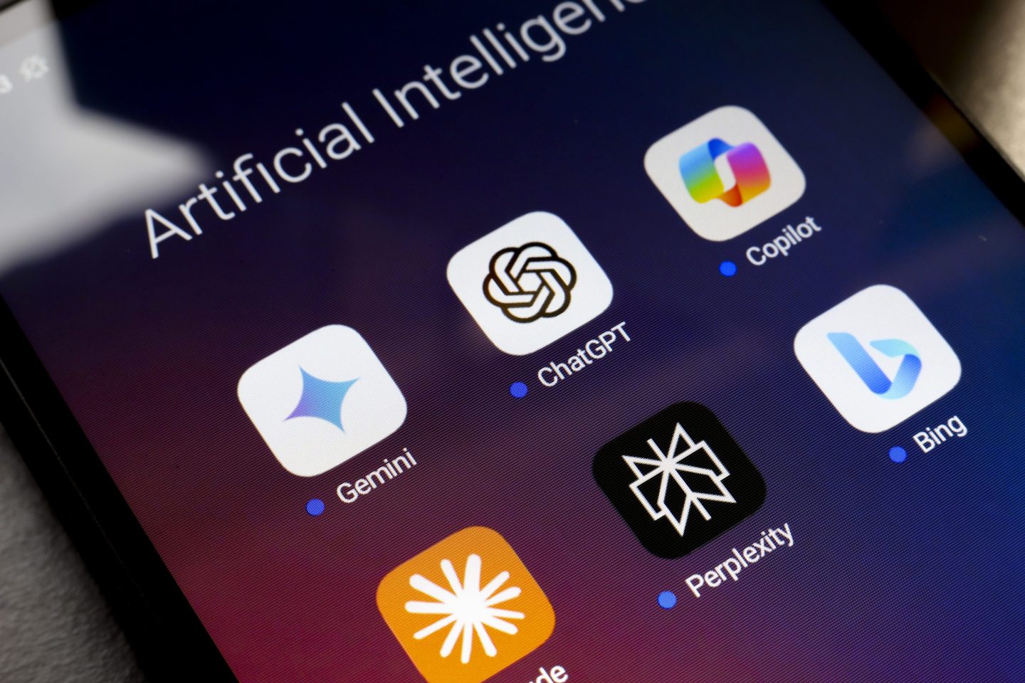 A smart phone screen displaying the app icons for a number of AI chatbots, including ChatGPT, Claude, Perplexity, Gemini, and others.