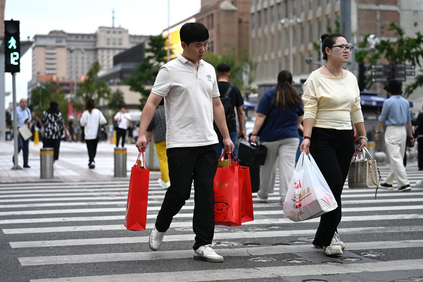 People carrying shopping bags while crossing a street in Beijing on September 15, 2025. China&#8217;s industrial production and retail sales growth slumped further last month, official data showed on September 15, missing forecasts and highlighting prolonged challenges in the world&#8217;s second-largest economy. (Photo by WANG Zhao / AFP) (Photo by WANG ZHAO/AFP via Getty Images)